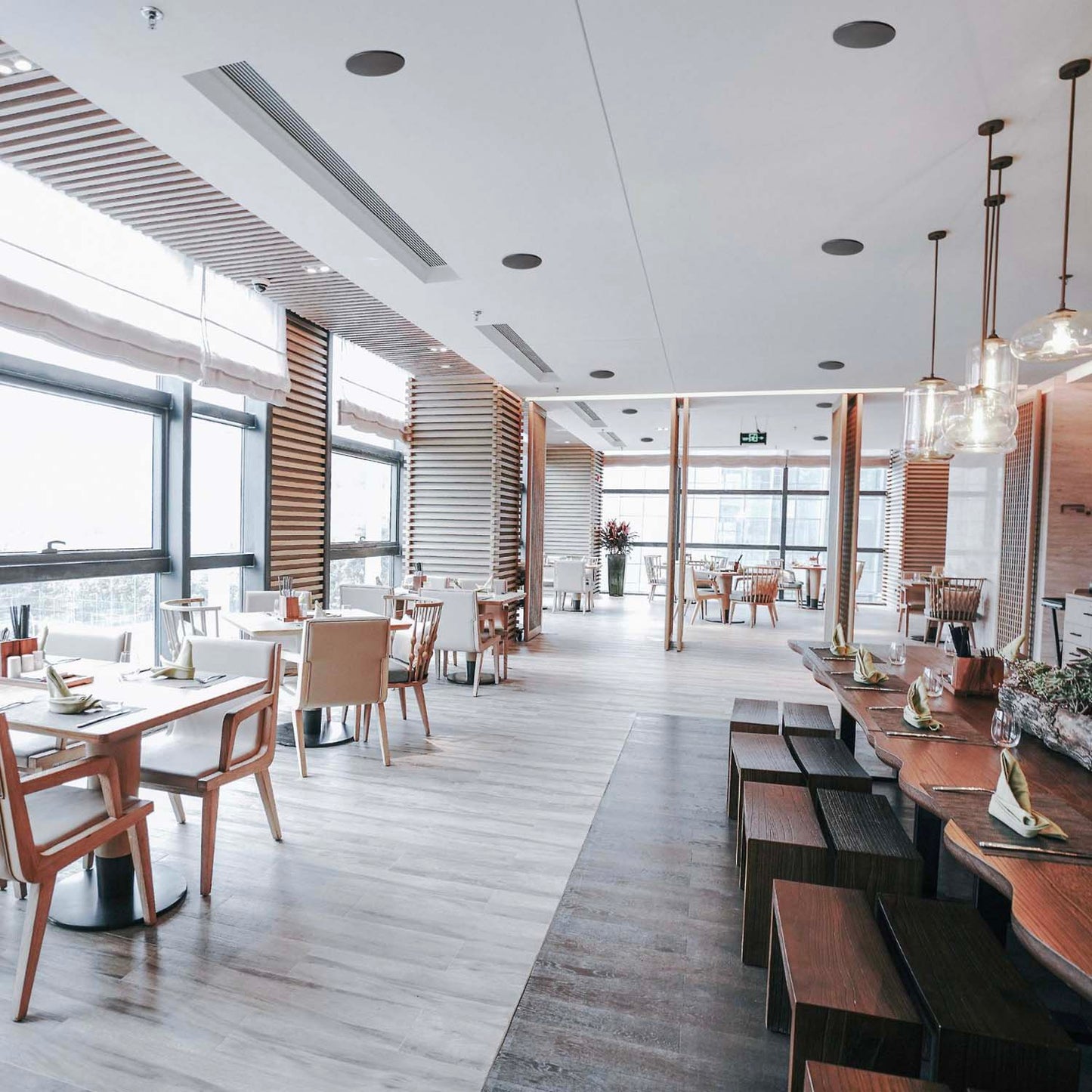Modern restaurant interior with wooden tables and chairs, large windows, and a sleek design.
