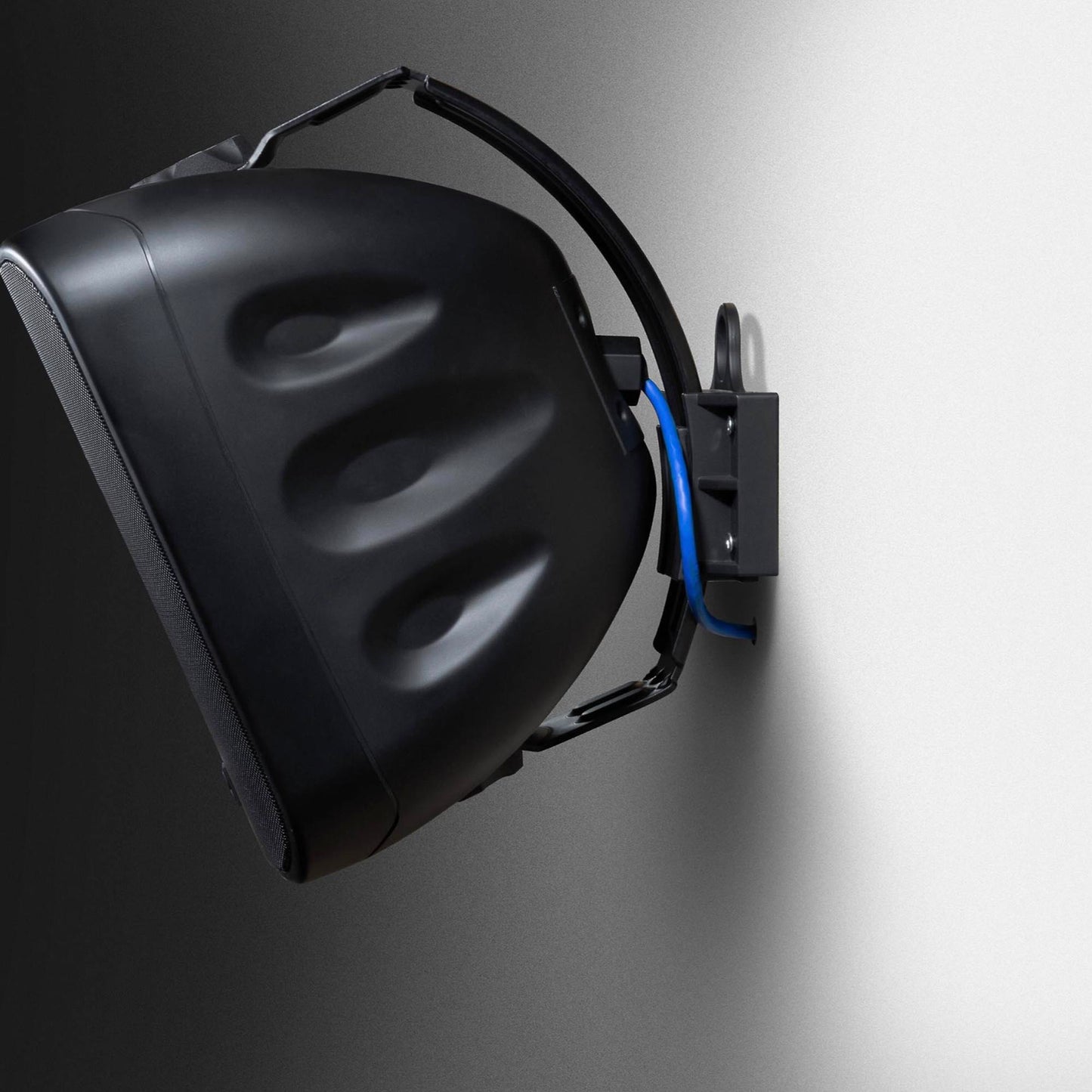 Black speaker mounted on a gray wall with blue wiring.