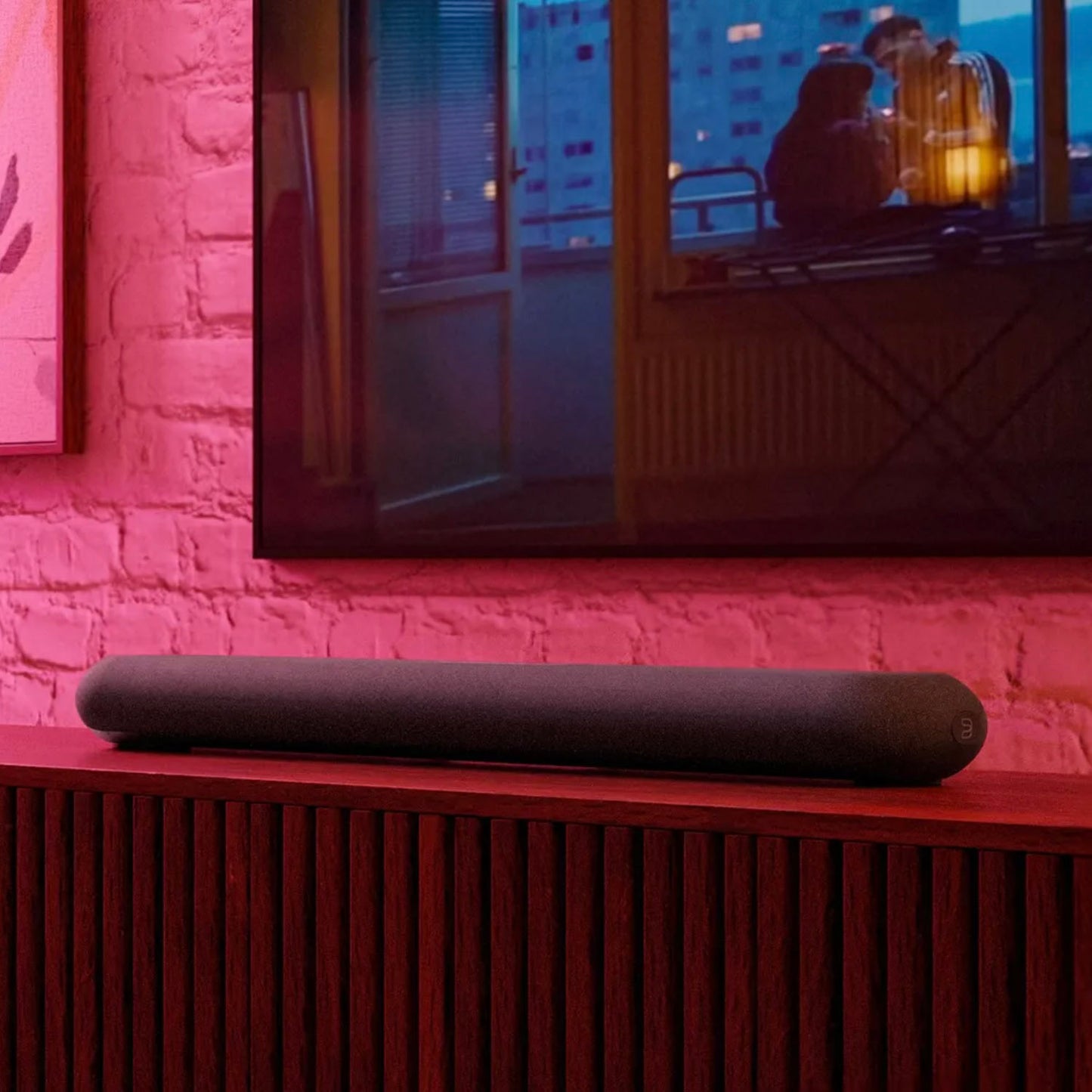 Soundbar on a wooden surface with a television displaying a romantic scene in the background.
