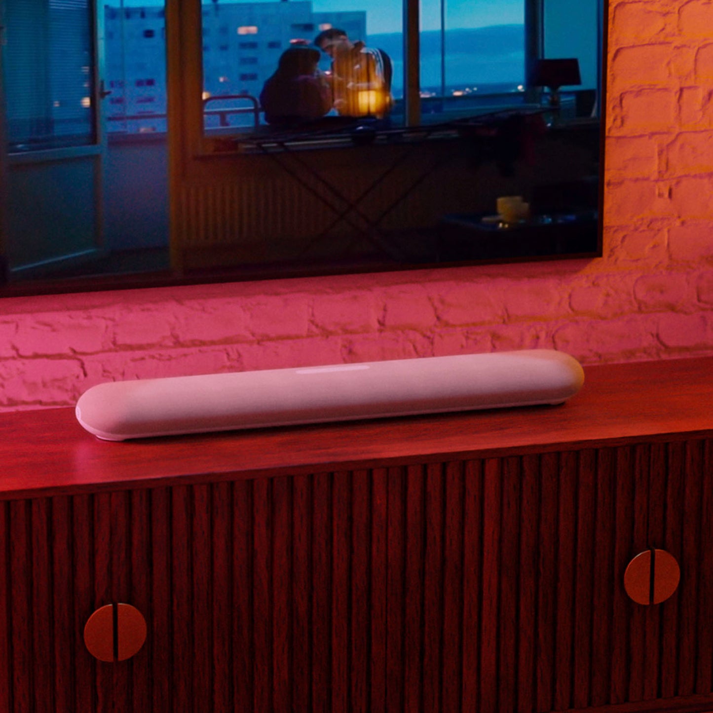 Soundbar on a wooden cabinet with a television displaying a cozy room scene in the background.
