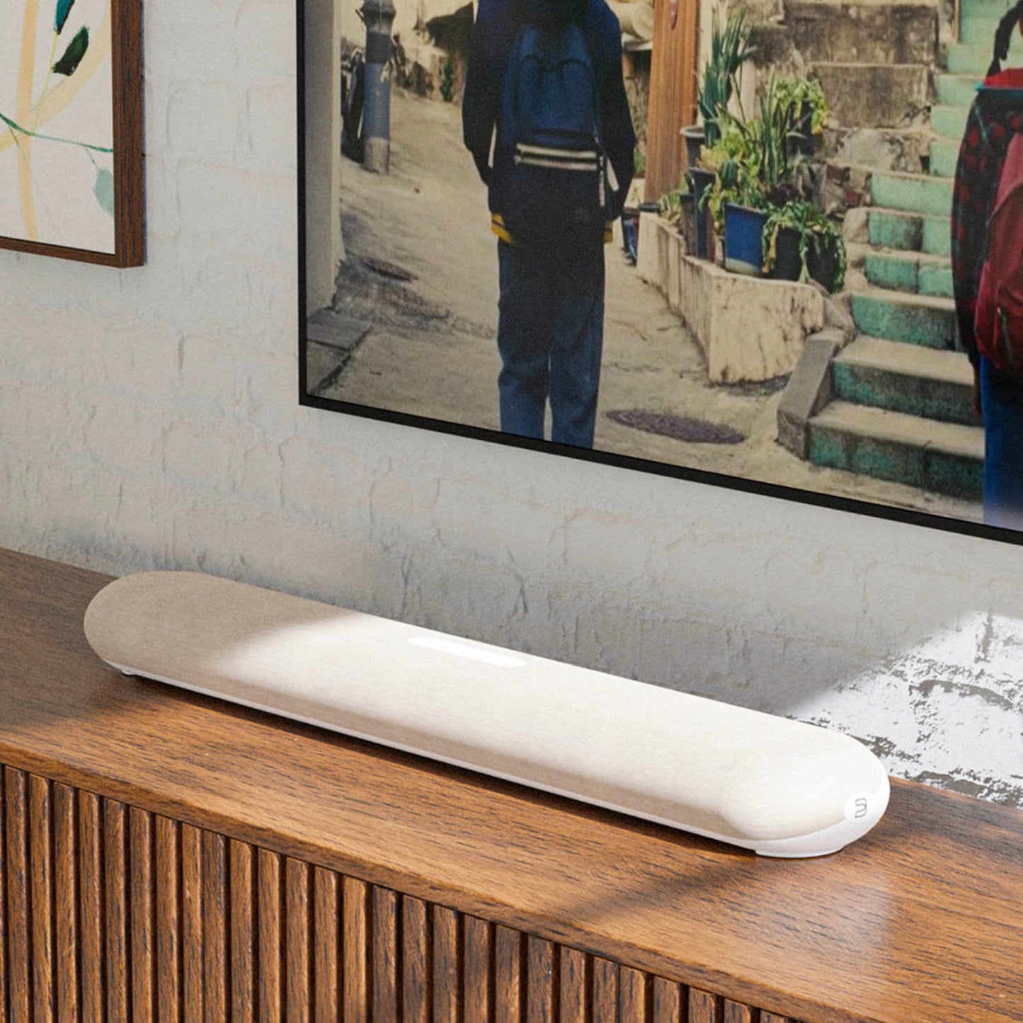 White electronic device on a wooden surface with a TV displaying an image of a person walking down a street.