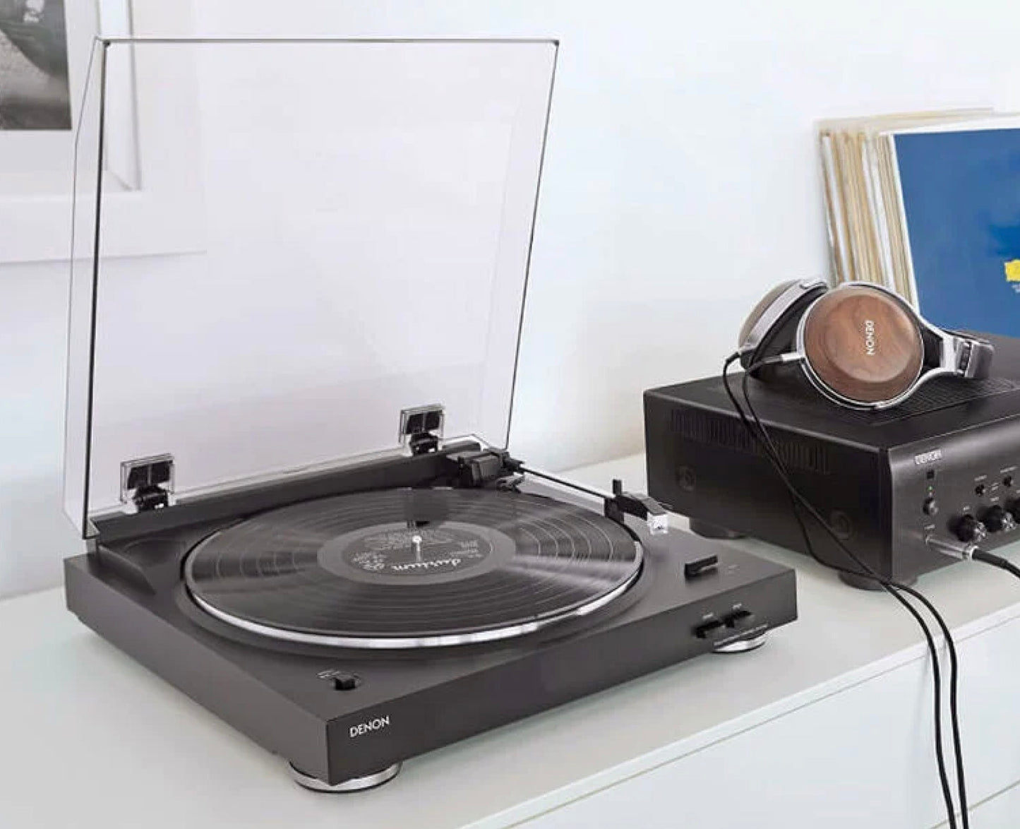 Denon turntable on a white surface with headphones and headphones in the background