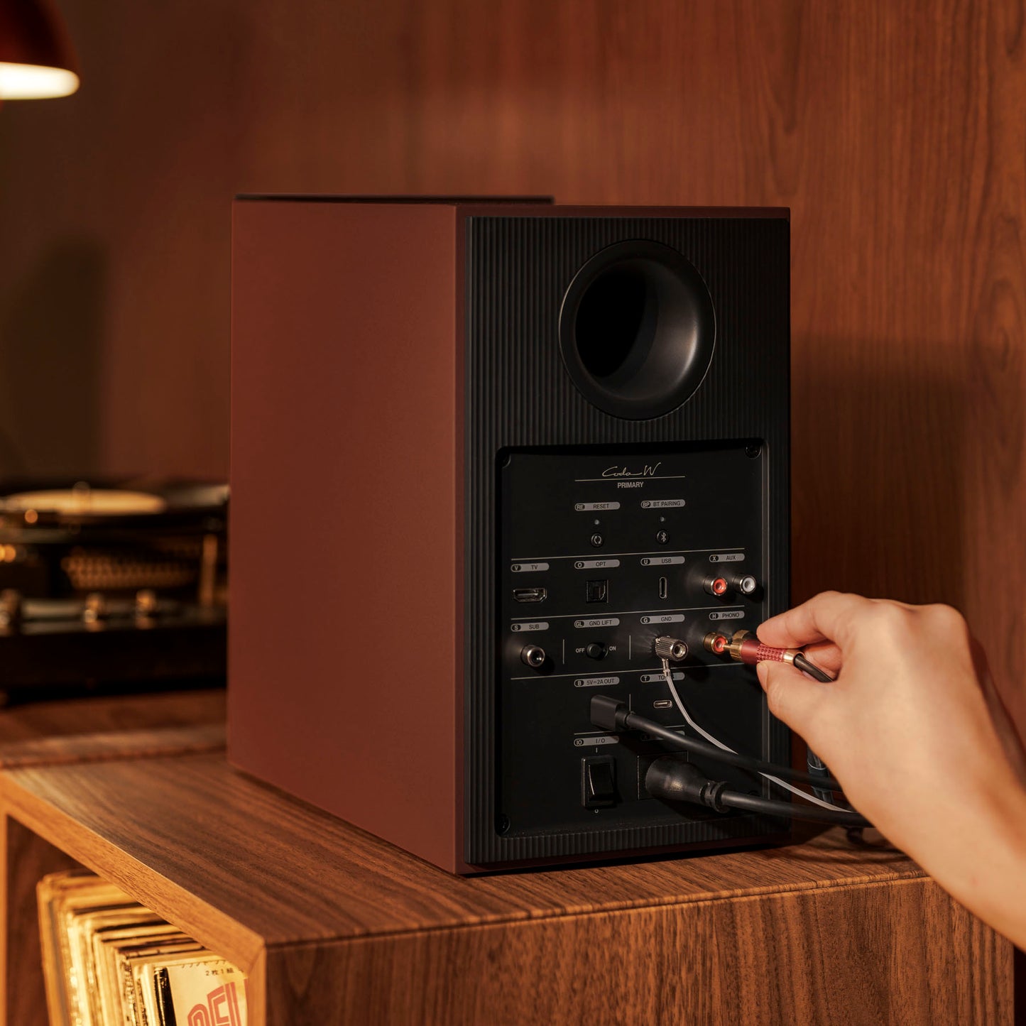 Person connecting audio cables to a speaker on a wooden surface.