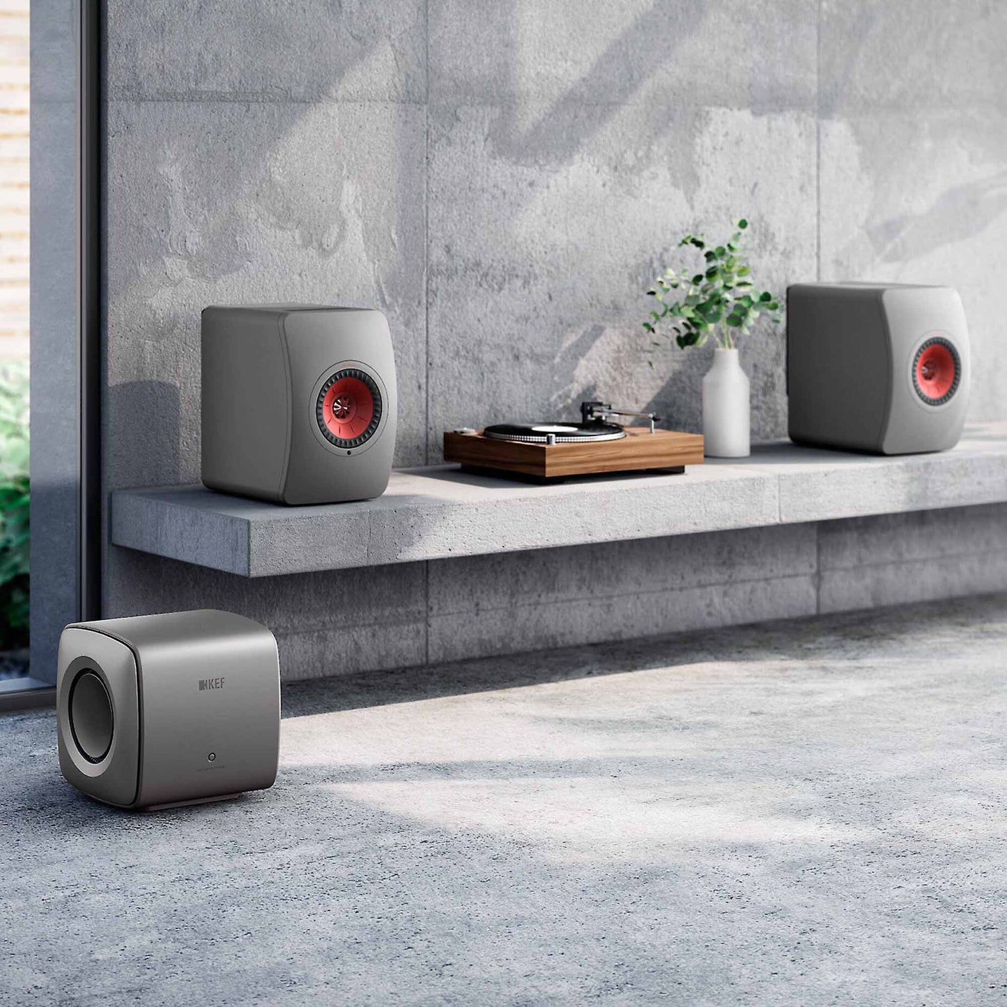 KEF KC62 Subwoofer in grey with a pair of KEF LS50 in grey on a shelf with a turntable