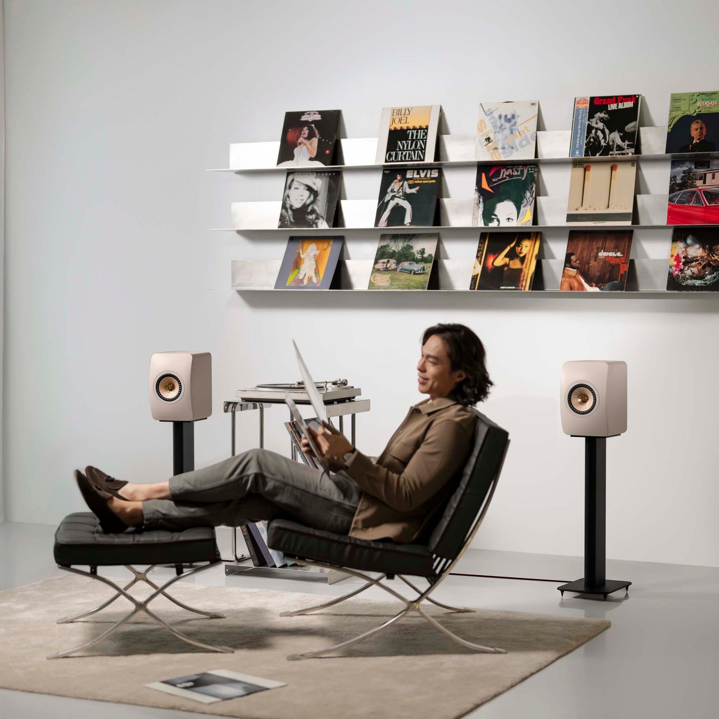 Person sitting in a modern chair with a laptop, surrounded by stylish speakers and a bookshelf with records.