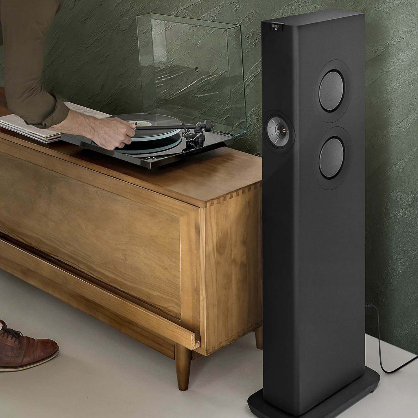 Black floorstanding speaker next to cabinet with turntable on it.