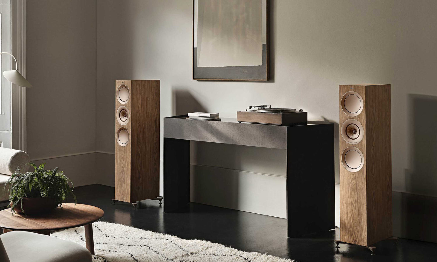 KEF R7 Meta floorstanding speakers in Walnut against wall next to grey table with turntable on it