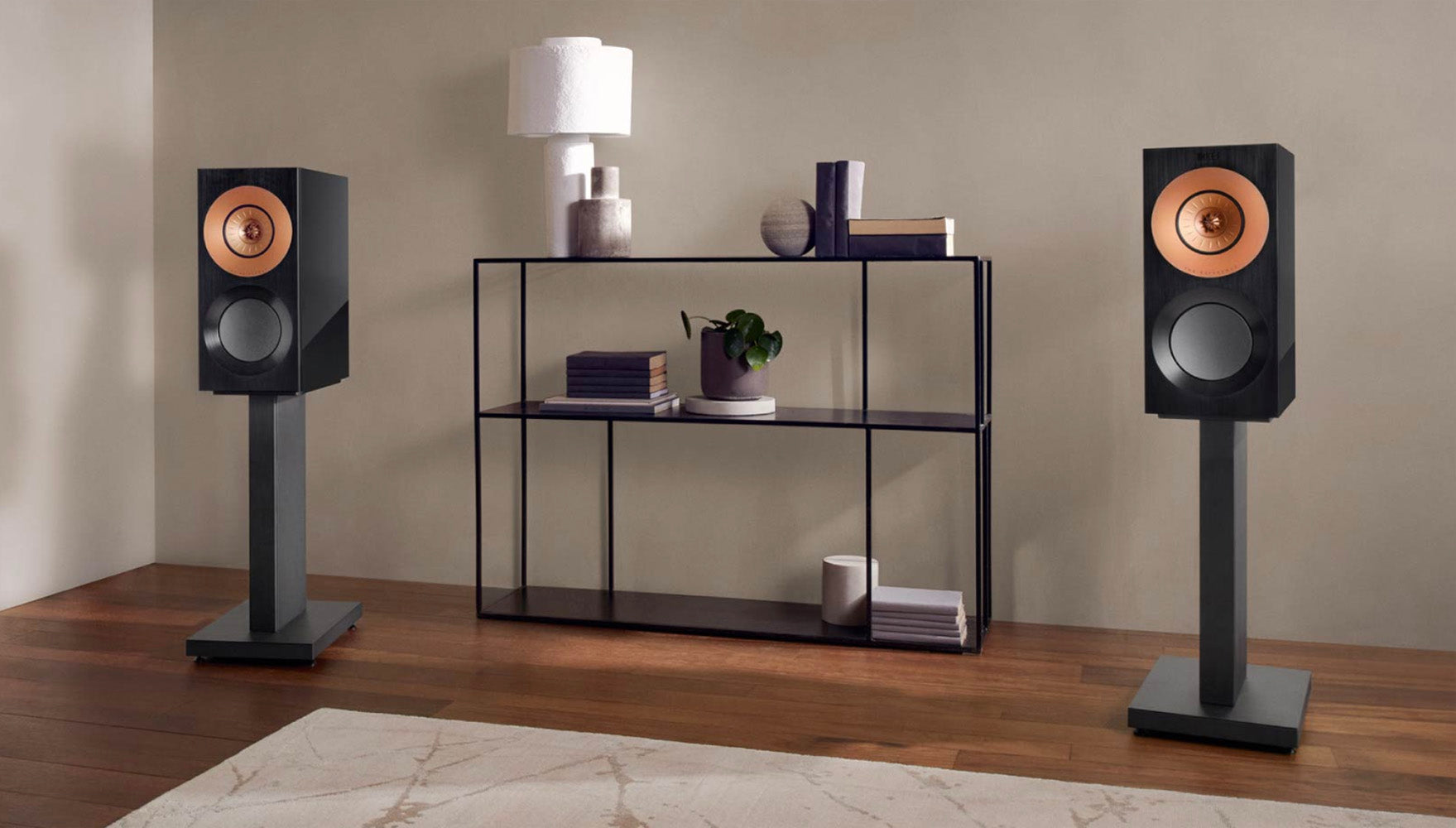 Pair of speakers on stands in a room with a shelf in the background