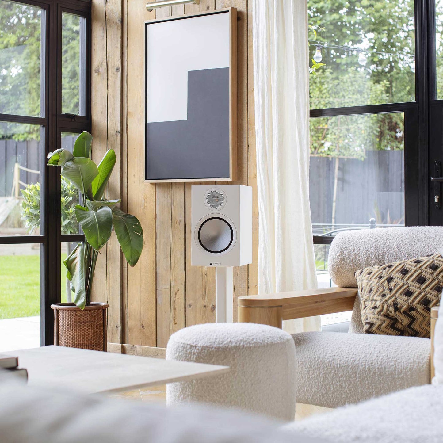 Modern living room with a white speaker, plant, and armchair.