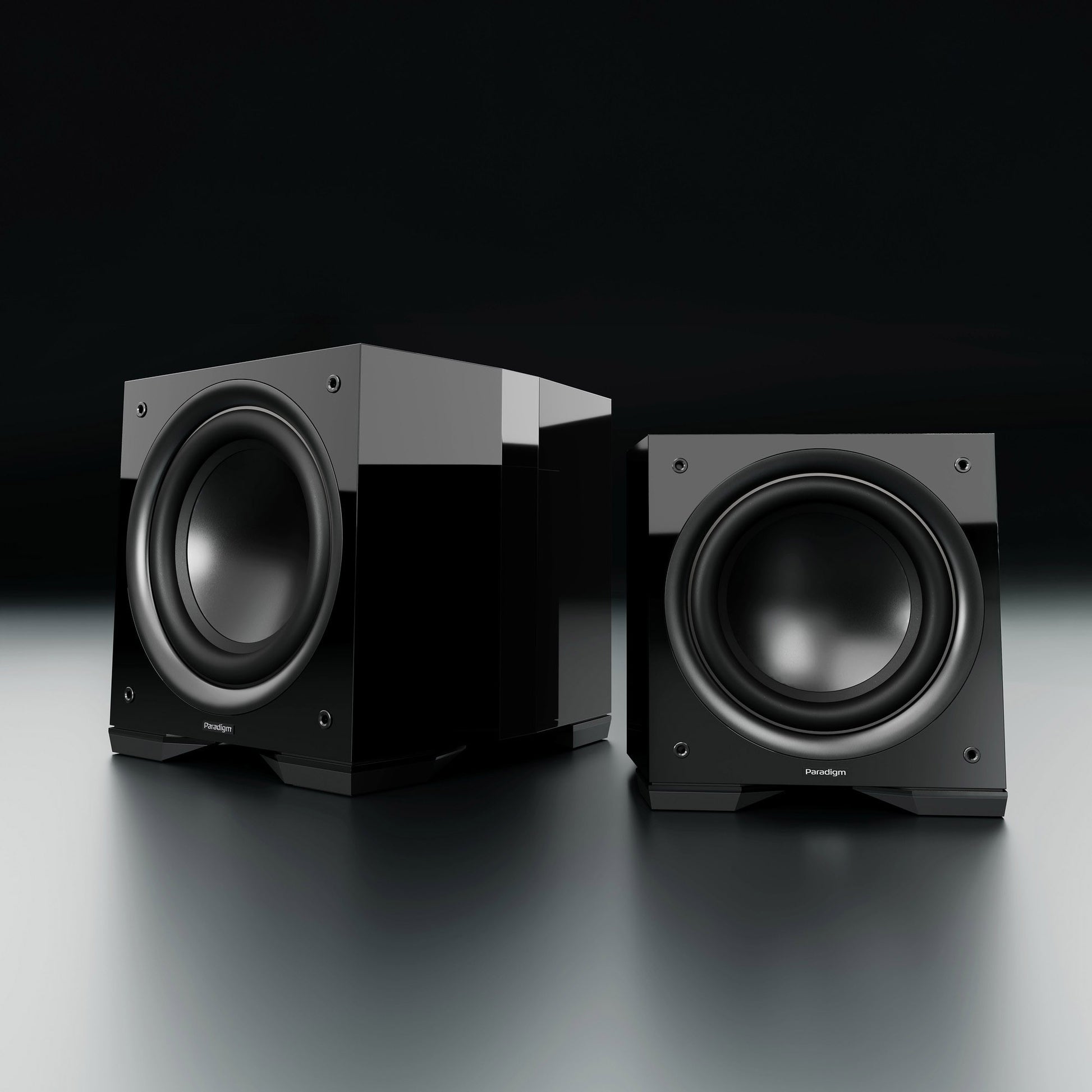 Two black subwoofers on a reflective surface with a dark background