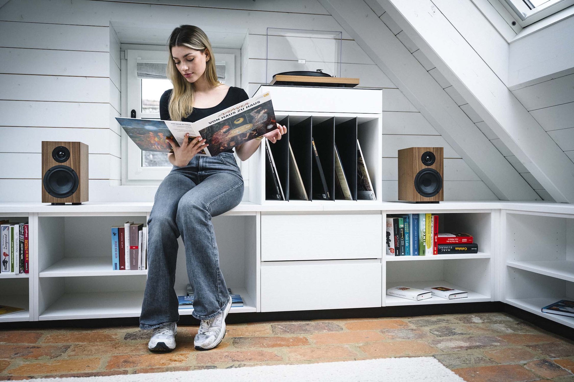 Woman reading a magazine in a room with white walls and tiled floor.