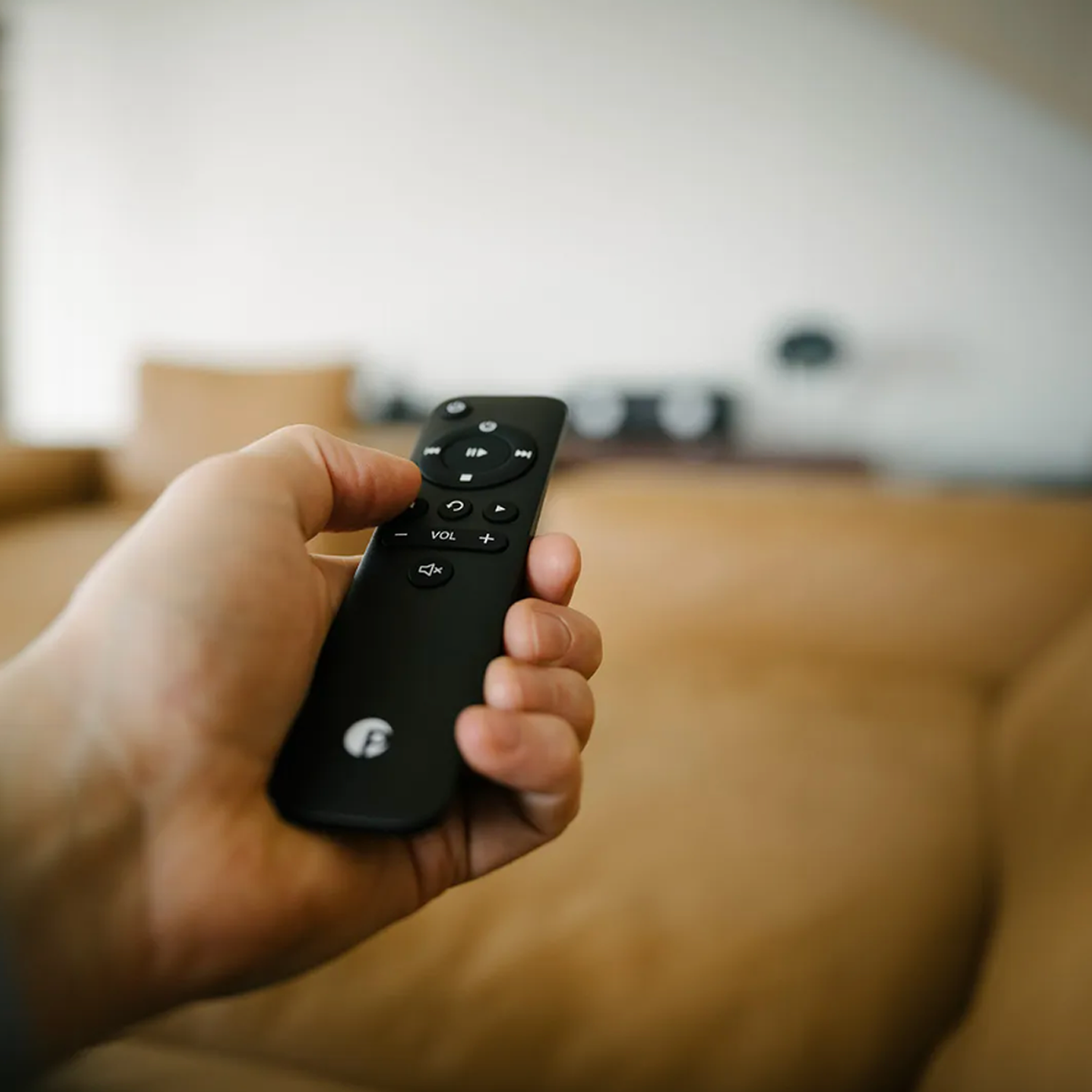 Hand holding a black remote control with a blurred indoor background