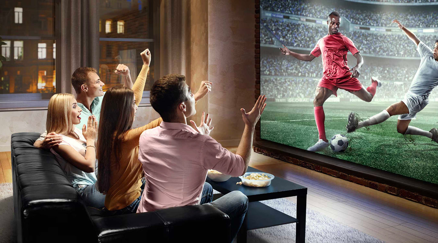 Group of people watching a soccer match on a large TV screen in a living room.