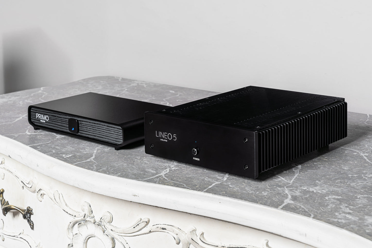 Two black audio equipment devices, displayed on a gray marble surface against a light gray wall.