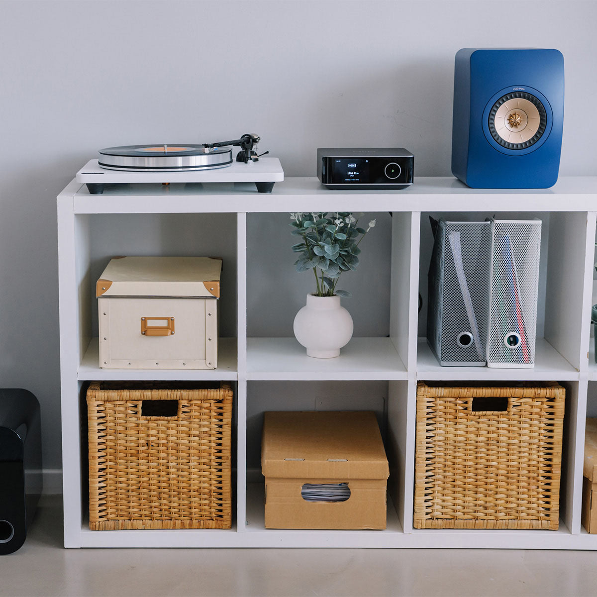 White storage shelf with various items including a blue speaker, record player, and decorative objects.
