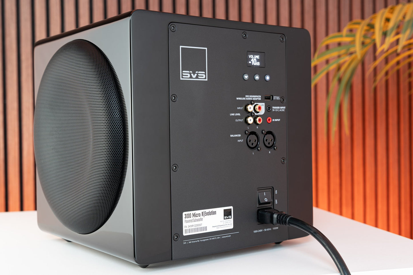 Black subwoofer with control panel on a white surface against an orange and brown striped background