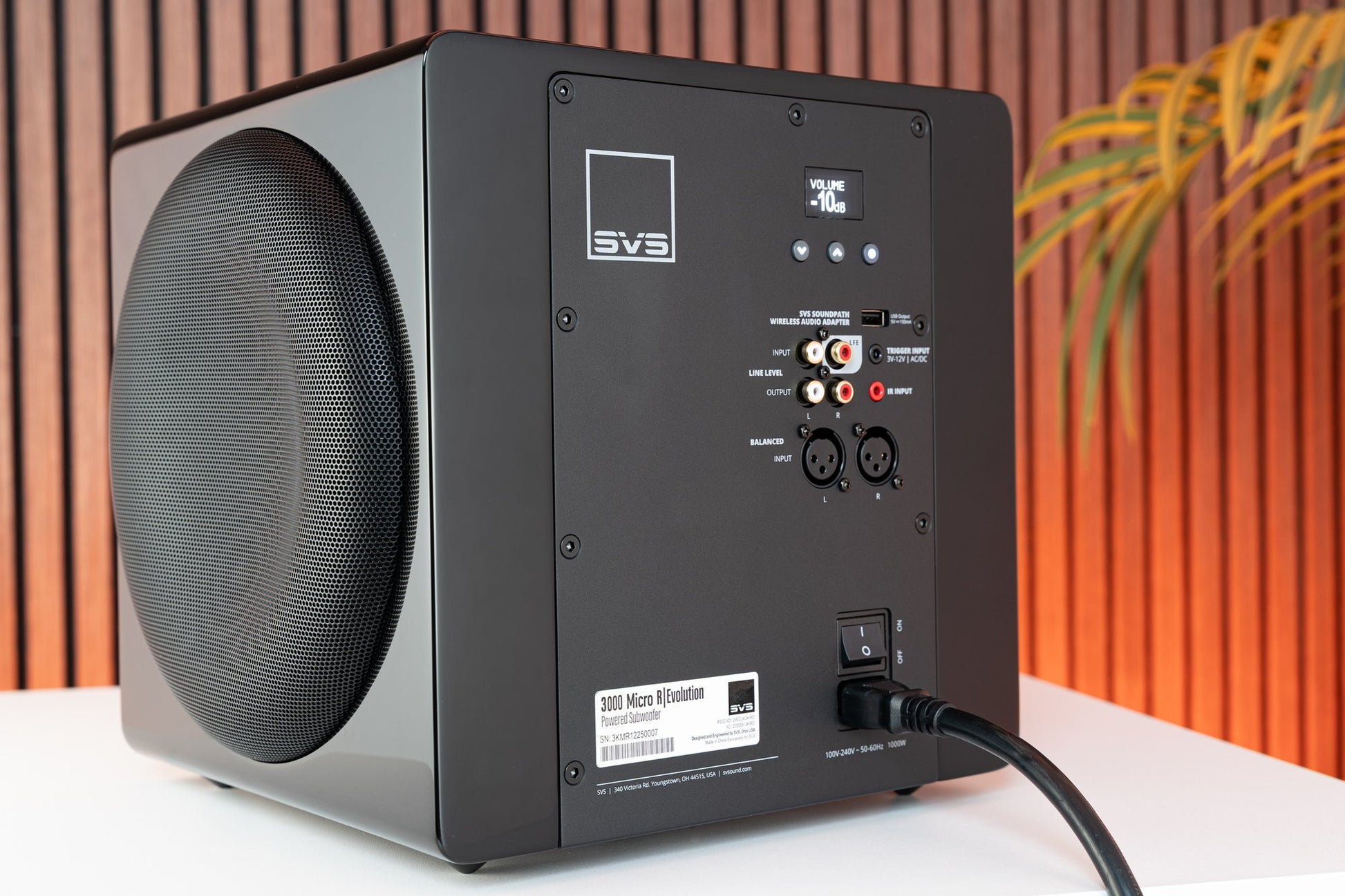 Black subwoofer with control panel on a white surface against an orange and brown striped background