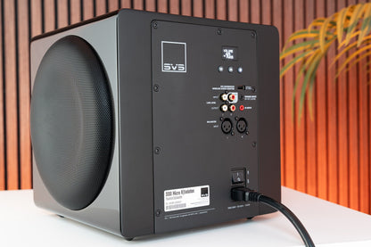 Black subwoofer with control panel on a white surface against an orange and brown striped background
