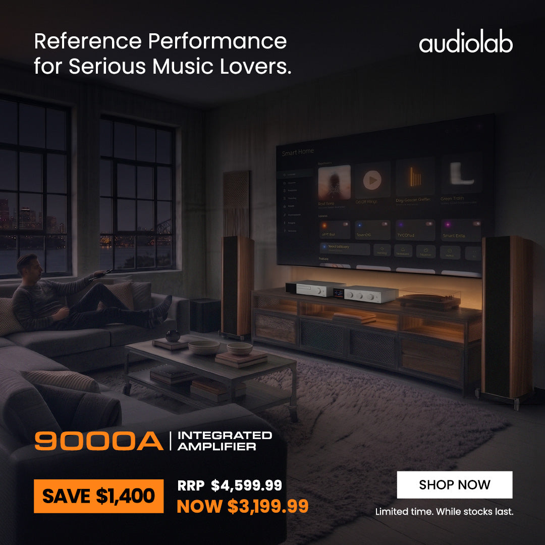 Audiolab 9000A integrated amplifier advertisement in a modern living room setting, showing a man relaxing on a couch, a large TV displaying the app, and the amplifier unit on a wooden media console.