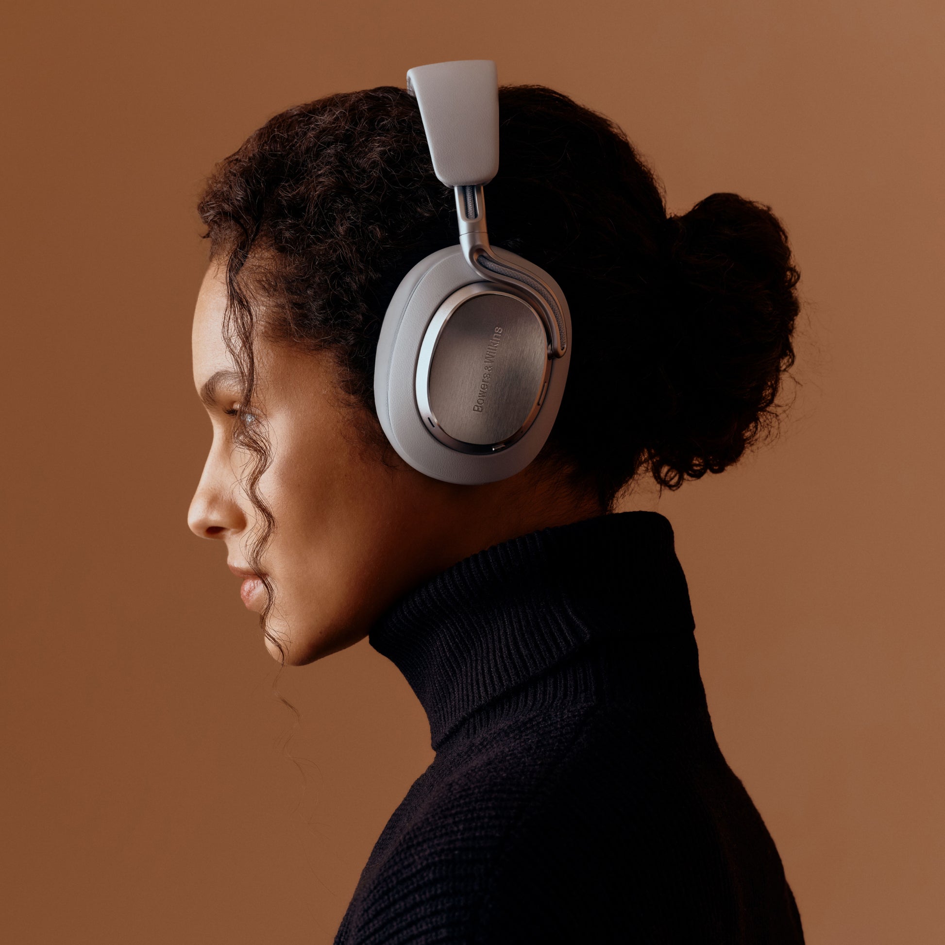 Lady with blad curly hair wearing Bowers & Wilkins PX8 Over-Ear Bluetooth Noise Cancelling Headphones in Pearl Blue
