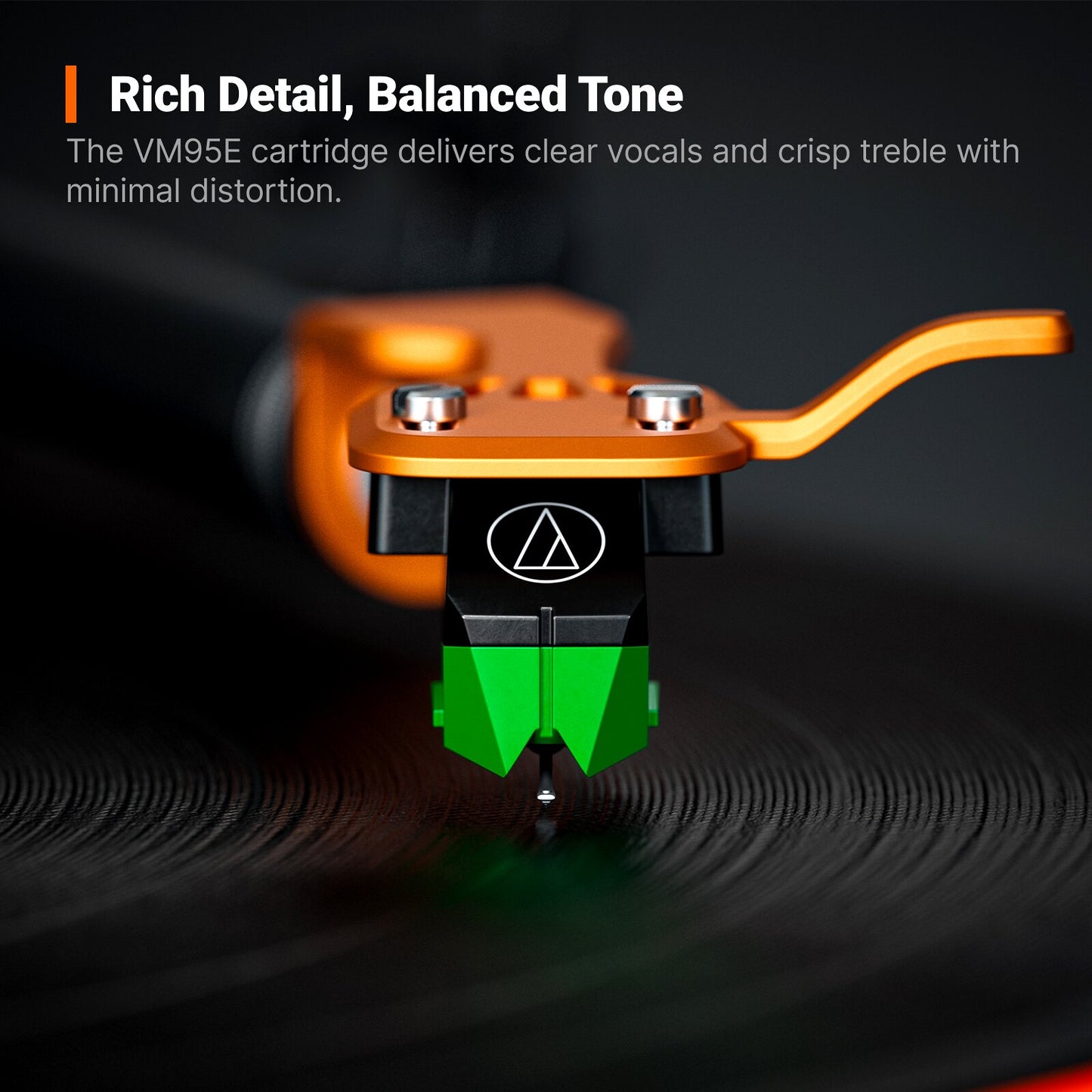 Close-up of a turntable needle cartridge resting on a vinyl record, with a bright orange tonearm and a black-and-green cartridge body. White marketing text at the top reads 'Rich Detail, Balanced Tone' and describes the VM9SE cartridge.