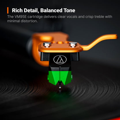 Close-up of a turntable needle cartridge resting on a vinyl record, with a bright orange tonearm and a black-and-green cartridge body. White marketing text at the top reads 'Rich Detail, Balanced Tone' and describes the VM9SE cartridge.