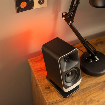 Speaker on a wooden surface with a lamp in the background