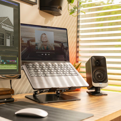 Laptop on a stand with two monitors, speakers, and a mouse on a desk.