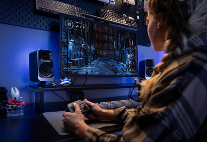 Person playing a video game on a computer setup with speakers and a monitor.