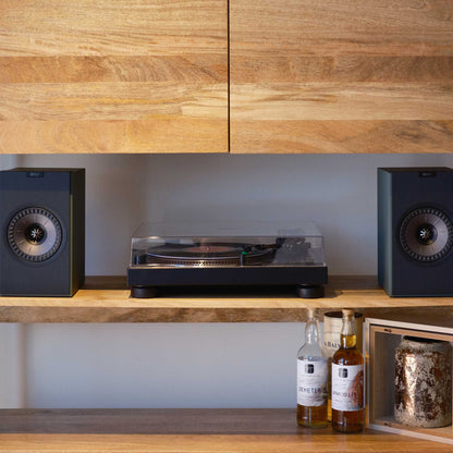 Turntable with speakers on a wooden shelf against a wooden wall.