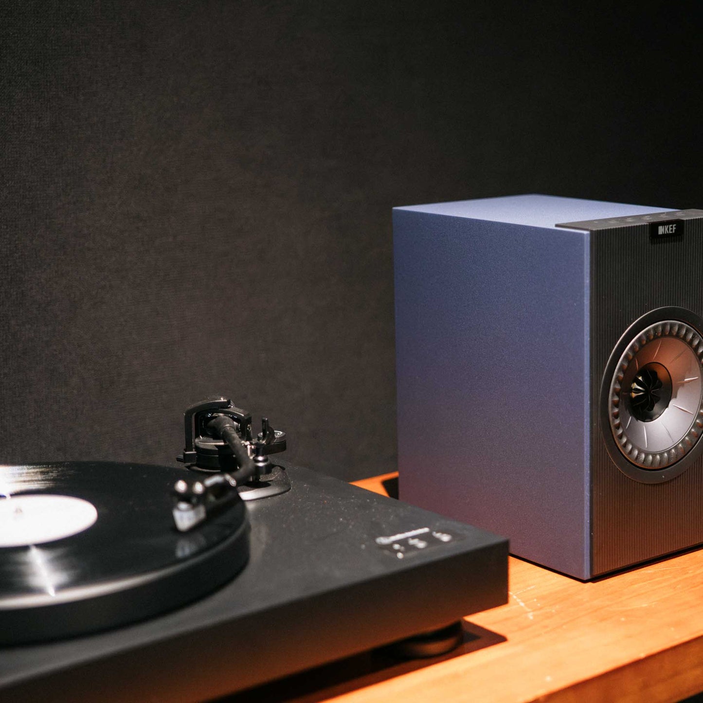 Turntable with a record and a speaker on a wooden surface against a dark background
