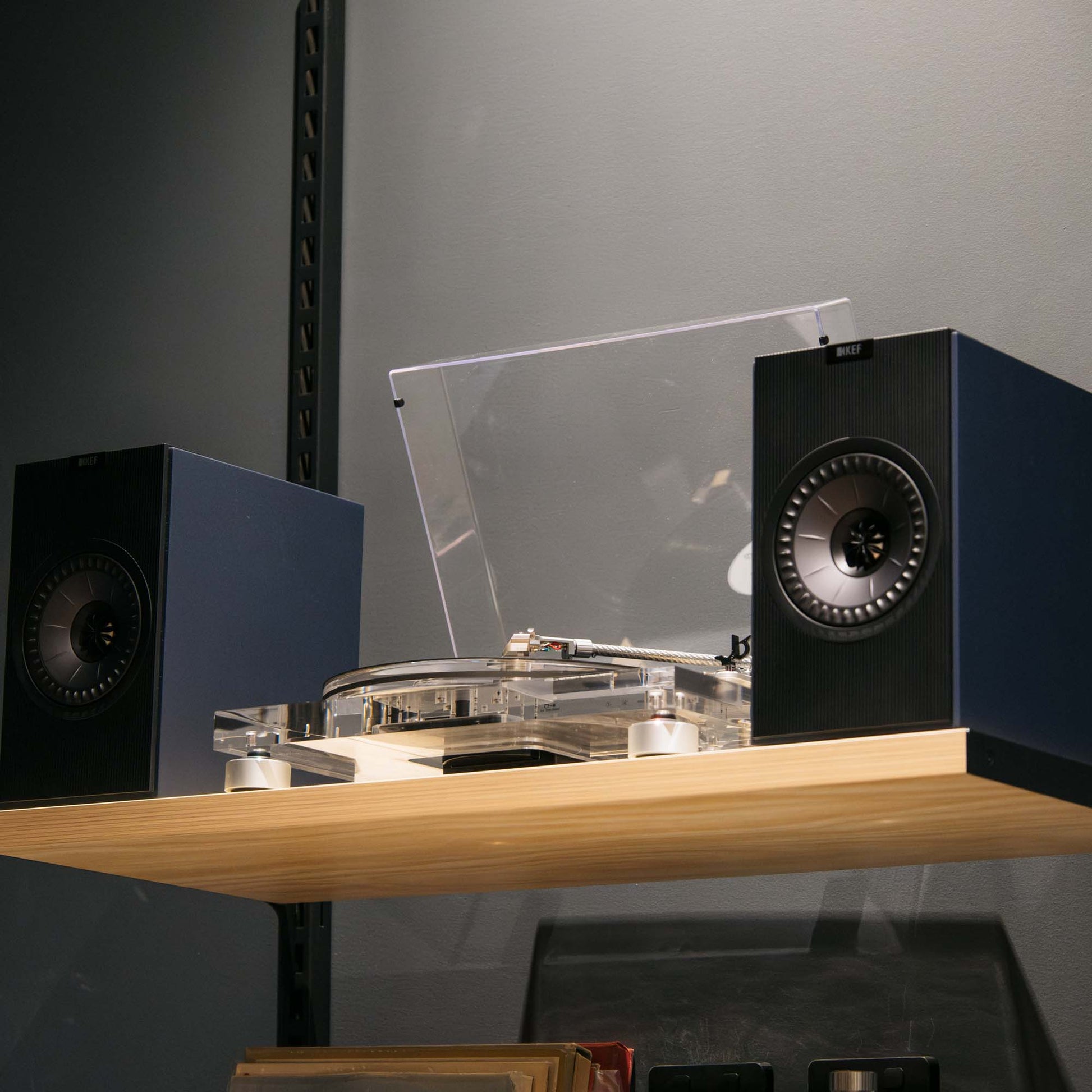 Turntable with clear turntable mat on a wooden surface with speakers in the background.