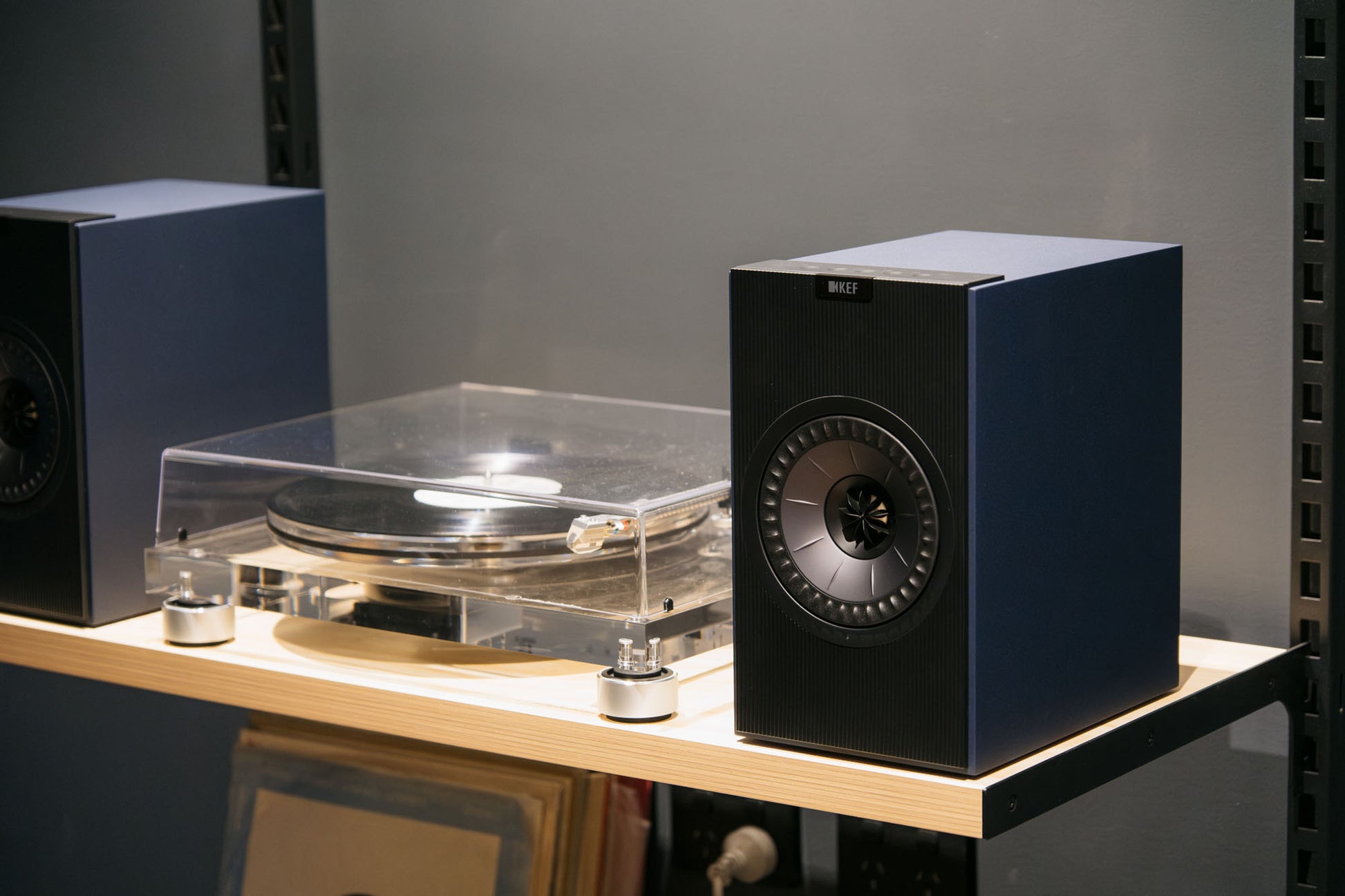 Pair of blue speakers on a wooden surface with a gray background