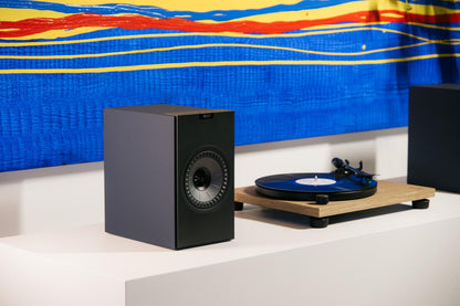 KEF Coda W Speaker and Audio Technica AT-LPW40WN Turntable on white shelf with bright artwork behind.