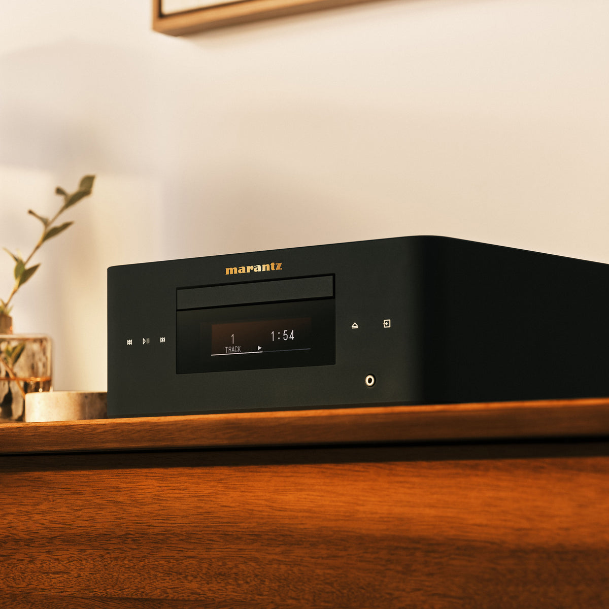 A Marantz CD player in matte black sits on a polished wooden console in a warm, softly lit room.
