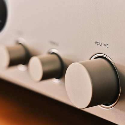 Close-up of a silver audio amplifier or receiver control panel with round volume and other knobs, including a prominent labeled 'VOLUME' knob.