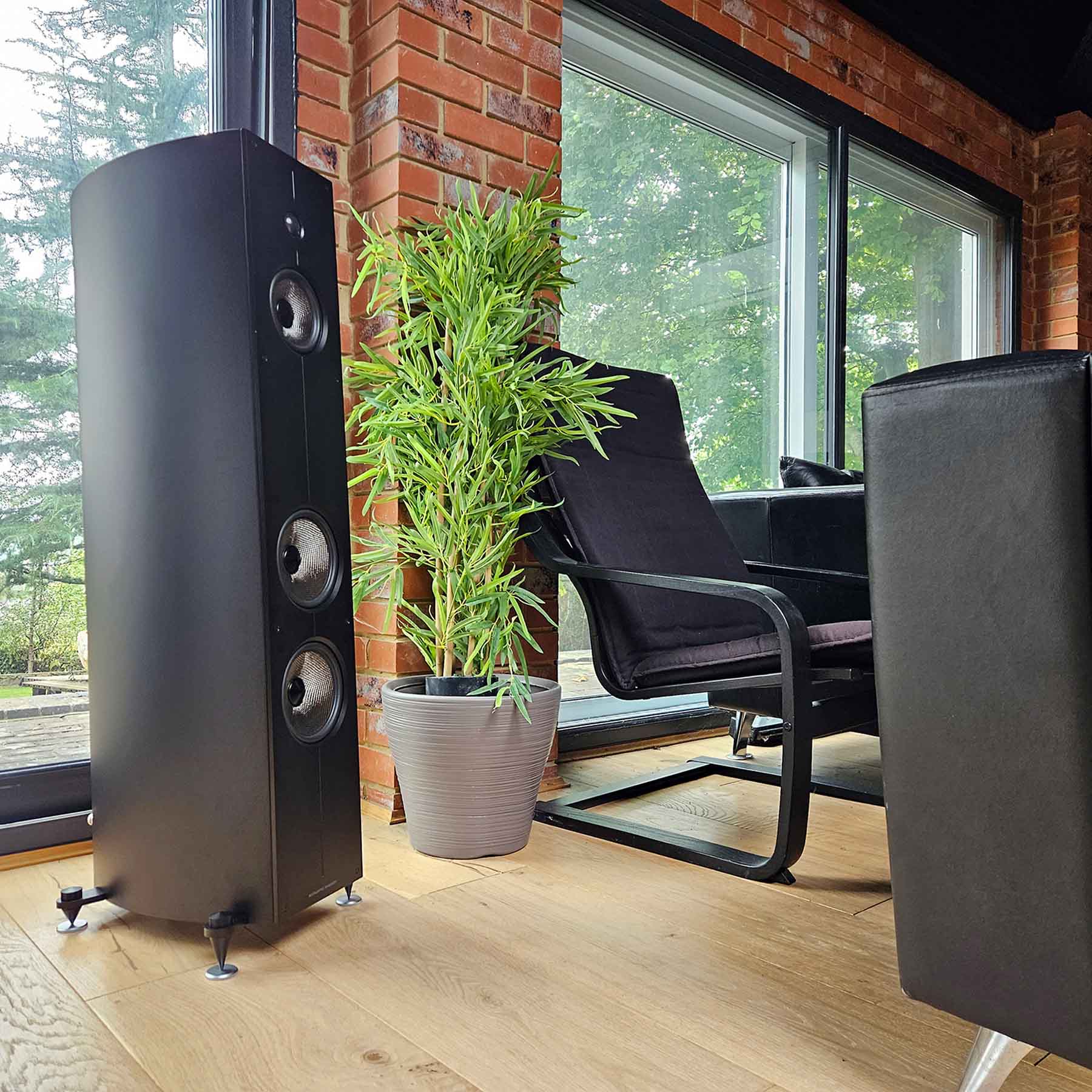 Black Acoustic Energy Corinium Speakers in modern living room next to a plant and black chair
