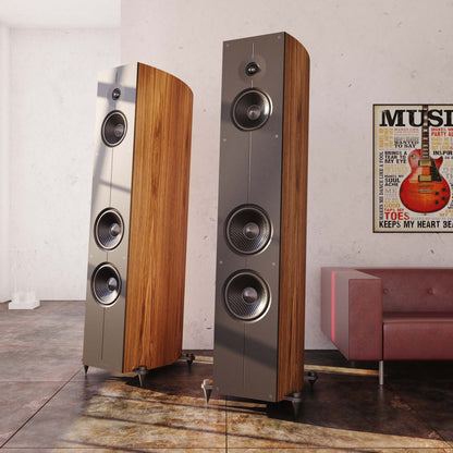Two tall floor-standing speakers in a room with a poster and sofa.