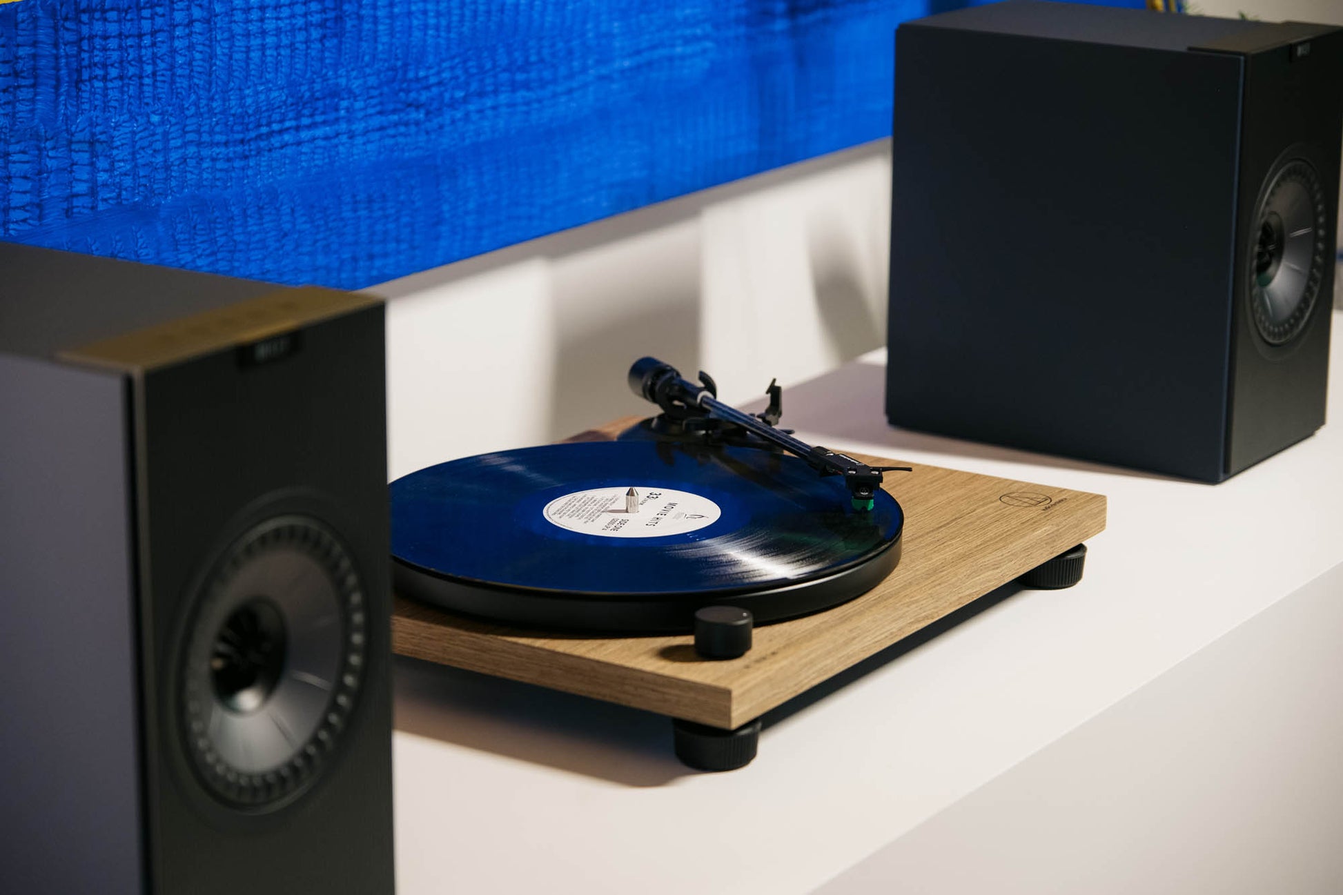KEF Coda W Speaker and Audio Technica AT-LPW40WN Turntable on white shelf with bright artwork behind.