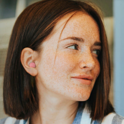 Close-up of a person with freckles and a pink earring, looking to the side.