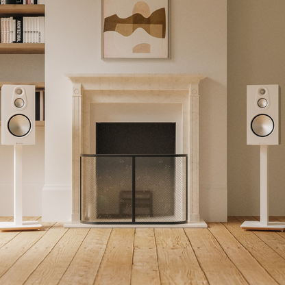 A pair of white floor-standing speakers flanking a cream stone fireplace in a modern living room with light wood floors and abstract wall art.