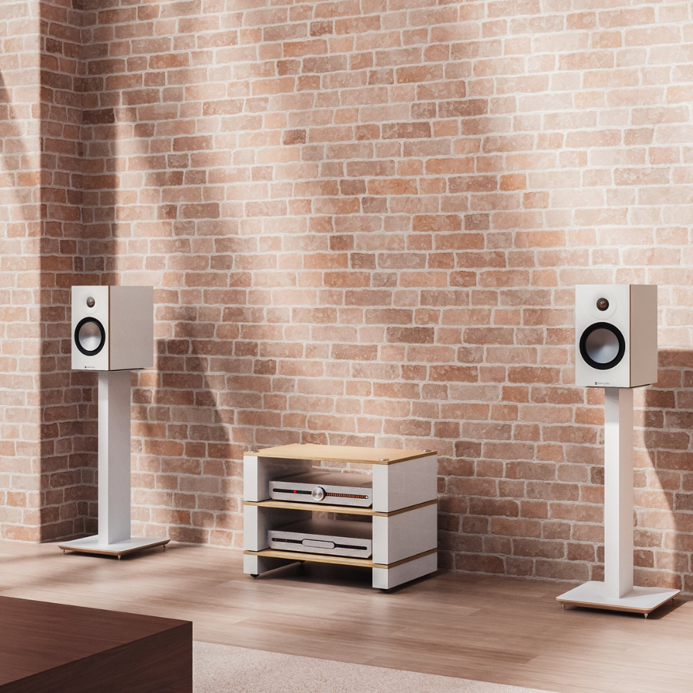 A pair of white floor-standing speakers on white stands flanking a small white and wood media console in front of a brick wall.