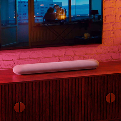 Soundbar on a wooden cabinet with a television displaying a cozy room scene in the background.