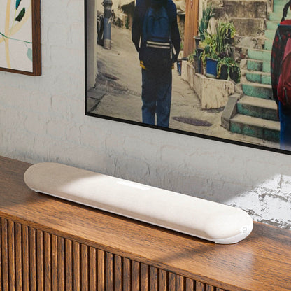White electronic device on a wooden surface with a TV displaying an image of a person walking down a street.