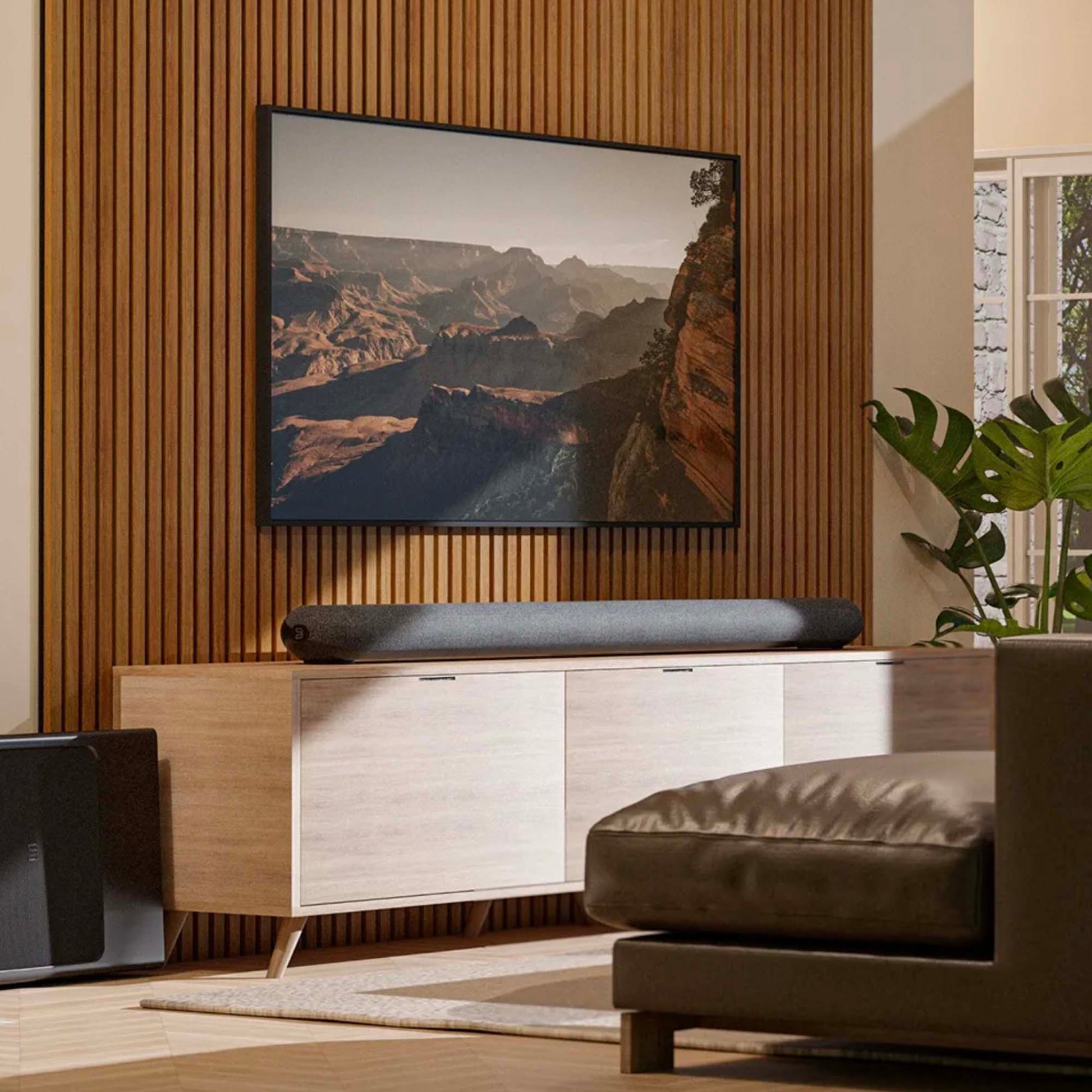 Modern living room with a flat-screen TV displaying a mountain landscape, wooden sideboard, and brown sofa.