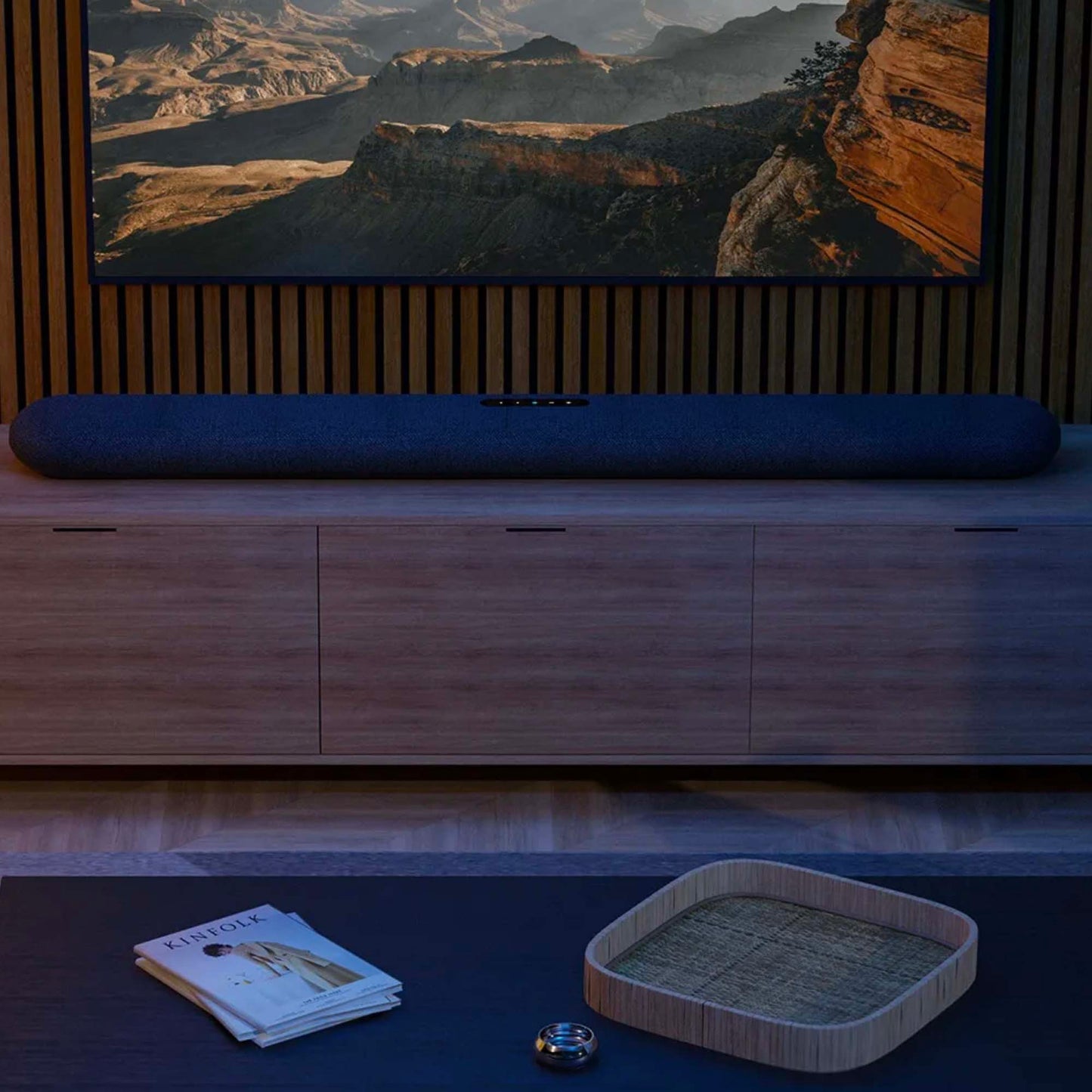 TV soundbar in front of a large screen displaying a mountainous landscape, with a wooden cabinet and decorative items below.