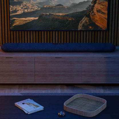 TV soundbar in front of a large screen displaying a mountainous landscape, with a wooden cabinet and decorative items below.