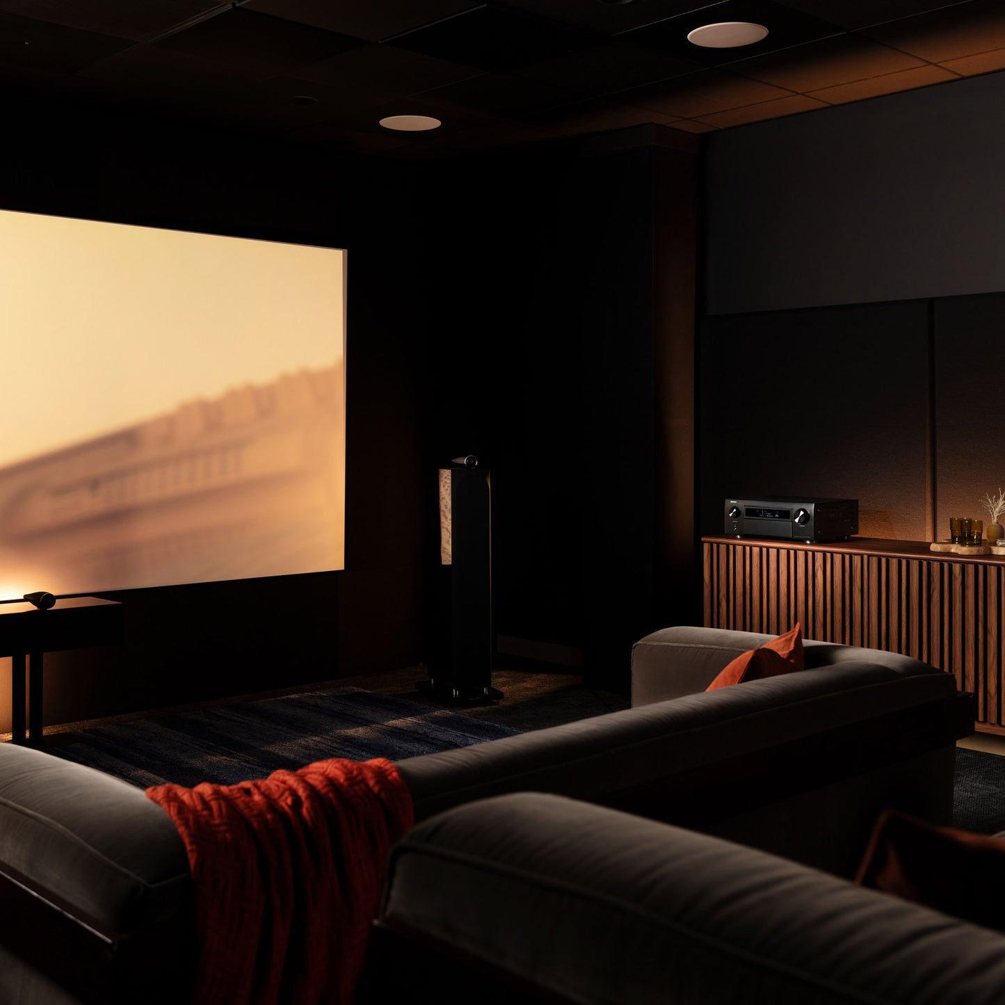 Home theater setup with a large screen displaying a scenic view, surrounded by comfortable seating and audio equipment.