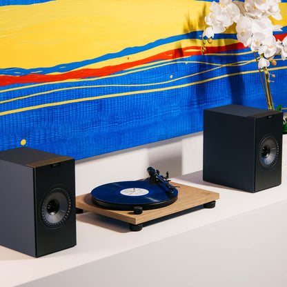 KEF Coda W Speaker and Audio Technica AT-LPW40WN Turntable on white shelf with bright artwork behind.