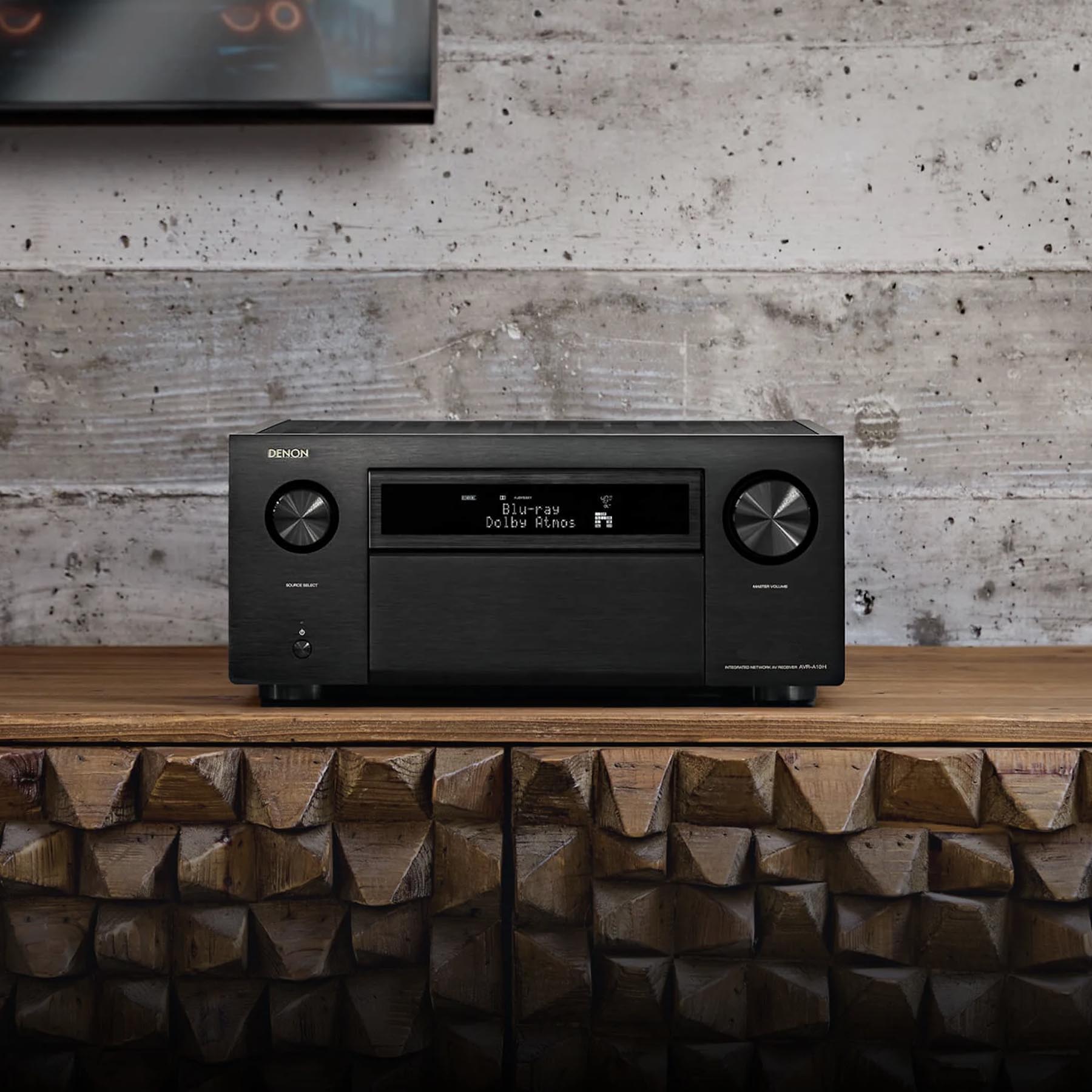 Black Denon audio receiver on a wooden shelf with a concrete wall background